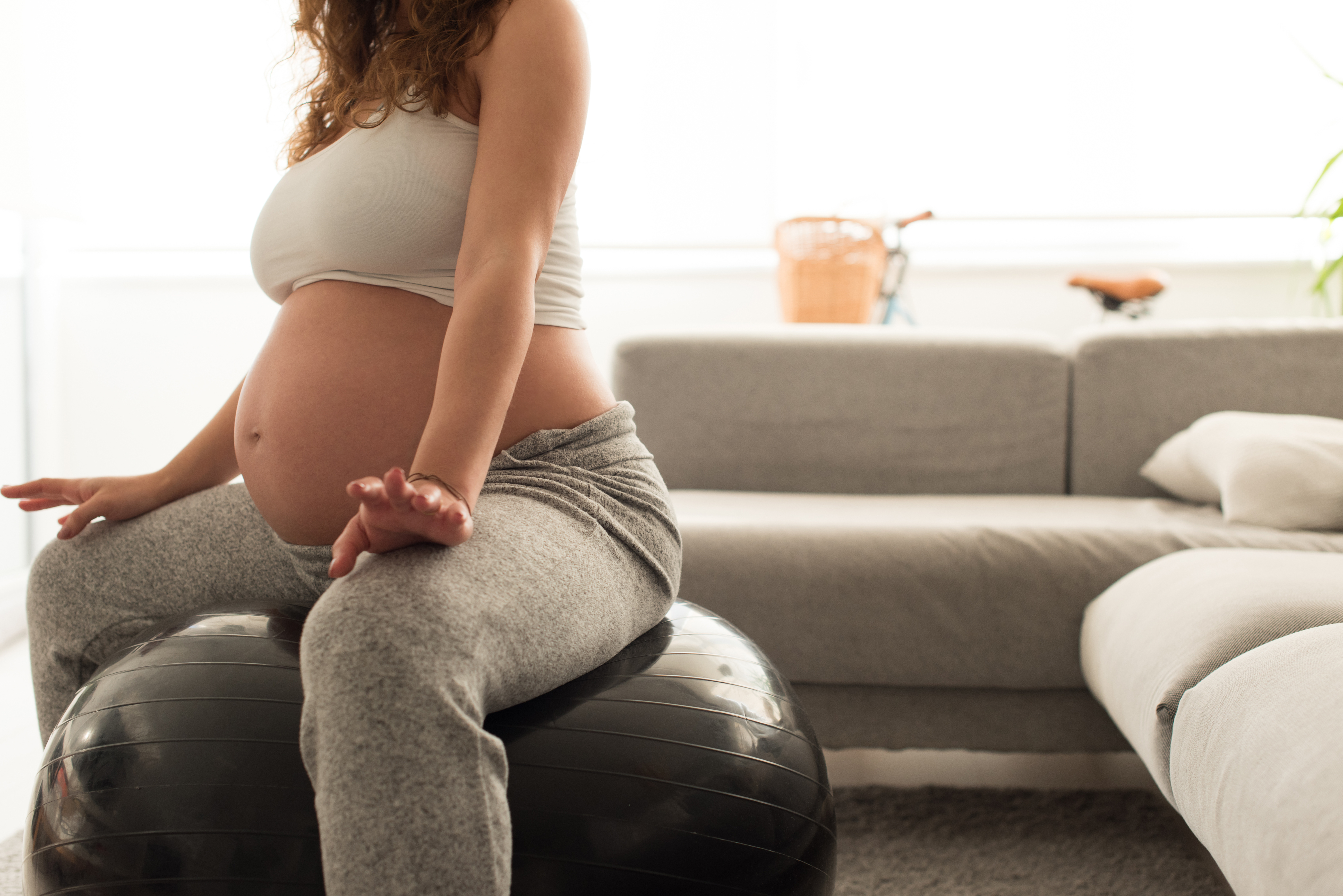 Femme enceinte assise sur un ballon de gym, en posture d’ouverture du bassin, illustrant la préparation physique à la naissance Femme enceinte assise sur un ballon de gym, en posture d’ouverture du bassin, illustrant la préparation physique à la naissance
